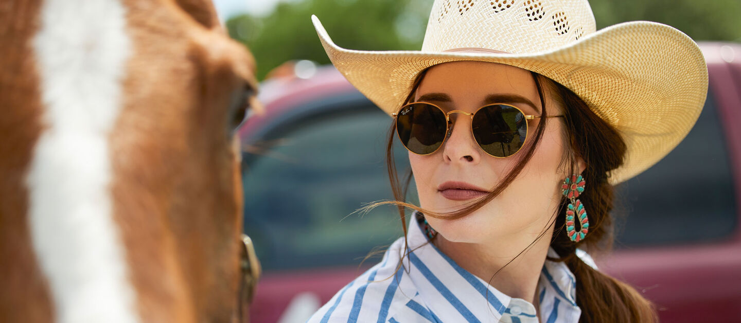 A woman staring wearing sunglasses leading a horse.